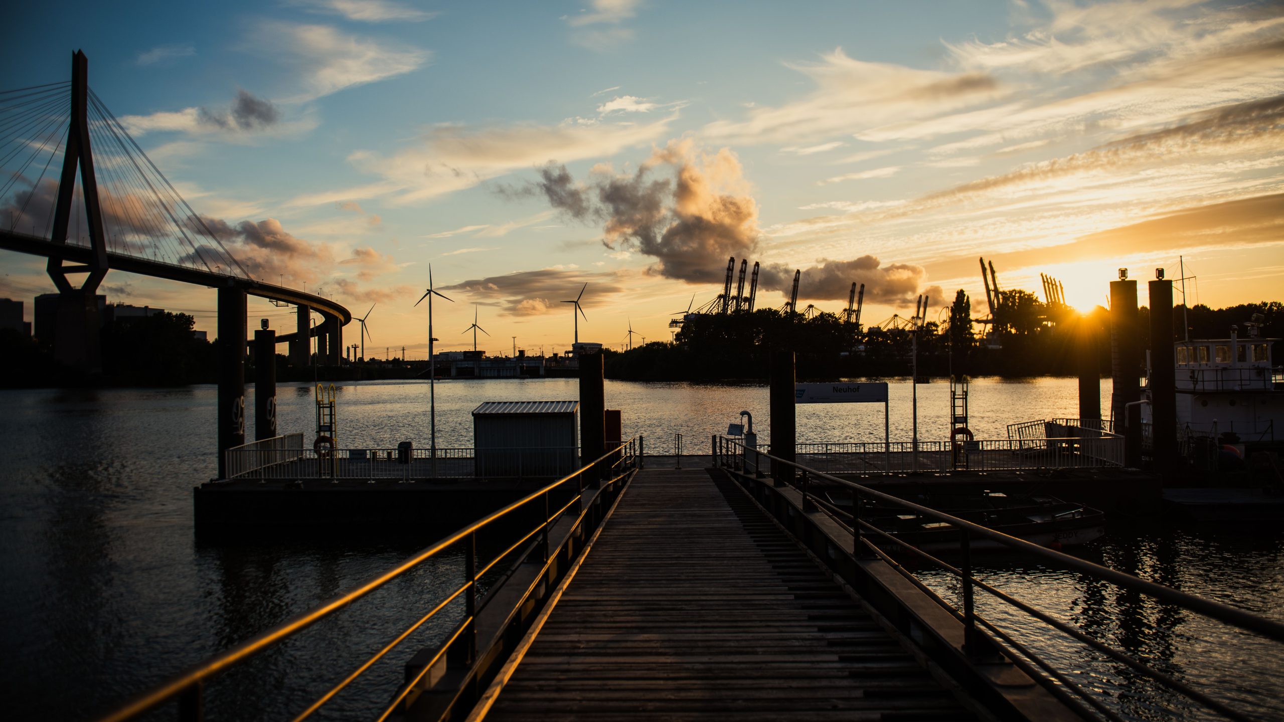 Sonnenuntergang über dem Hamburger Hafen mit Kränen und einem Steg